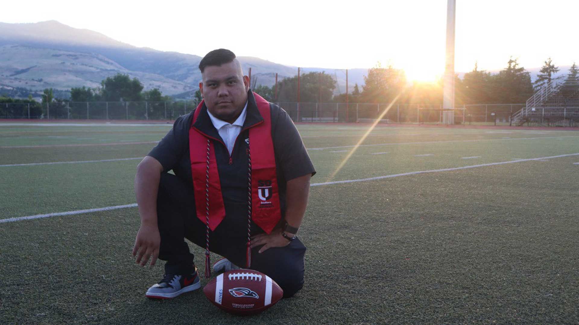 SOU Graduate Spotlight Jose Angel Stephen-Herman kneeling on football field at Southern Oregon University